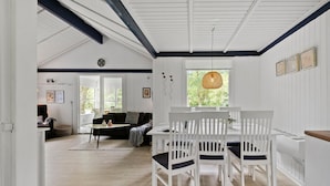 A spacious room with a dining area featuring a white table and chairs, a sofa, and a large window with a view of greenery. - Nice home in Hemmet with WiFi (Hemmet)