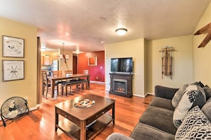 A living room with a wooden floor, a sofa, a dining table with chairs, a fireplace, and a television.