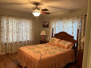 Un dormitorio con cama, cortinas, ventilador de techo, mesita de noche y lámpara.