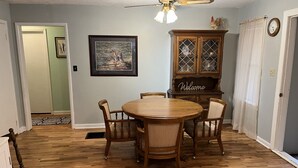 A dining area with a wooden table and chairs, a ceiling fan, a framed picture, and a cabinet with a 'Welcome' sign. - Cozy home with easy access to the main highway thru town, but in quiet area.  (Laverne)