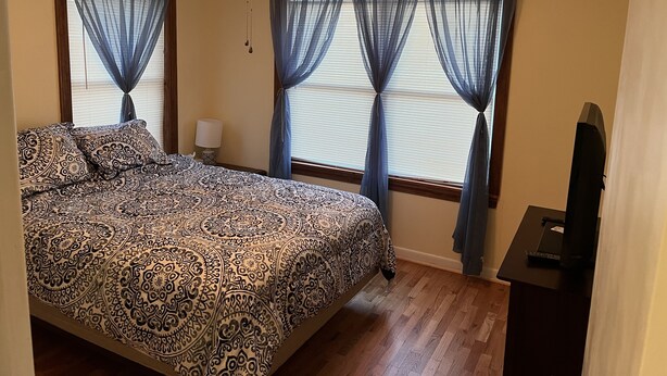A bedroom with a bed, a ceiling fan, and two windows with sheer curtains. - Cozy home with easy access to the main highway thru town, but in quiet area.  (Laverne)