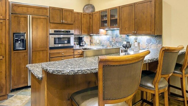 A kitchen with wooden cabinets, a granite countertop, stainless steel appliances, and bar stools. - Aspen | Luxury Ski Retreat | Pool + Ski (Aspen)