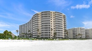 A multi-story hotel with a curved facade, located adjacent to a sandy beach. - Crystal Sands Beach Elegance (Siesta Key)