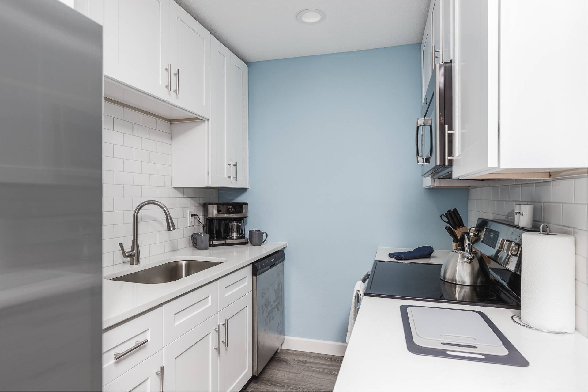 A compact kitchen with white cabinets, a coffee maker, and a sink.
