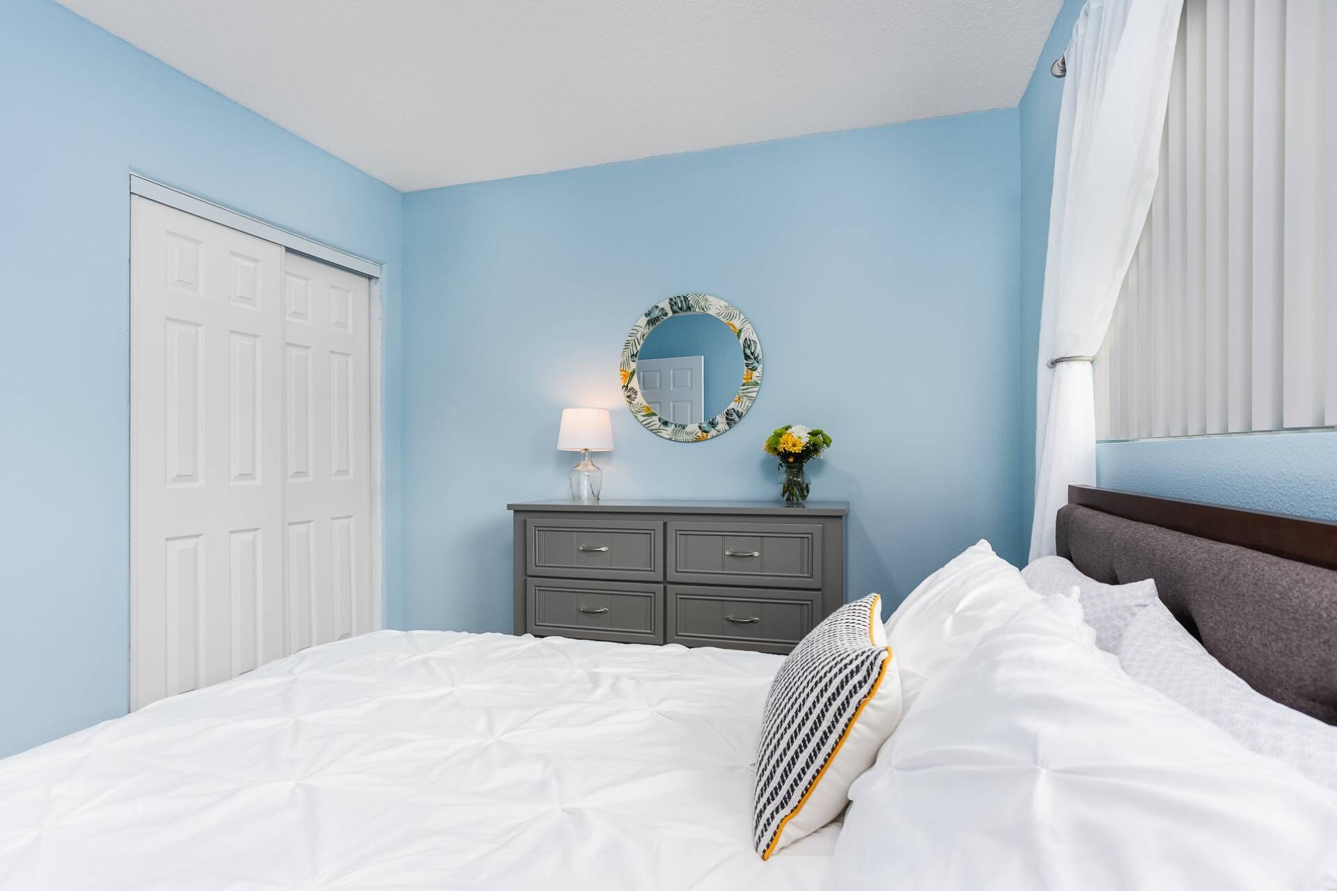 Quarto com uma cama, cômoda, espelho e janela com cortinas.