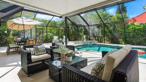 Uma área externa coberta com piscina, móveis de vime e uma mesa com tampo de vidro.