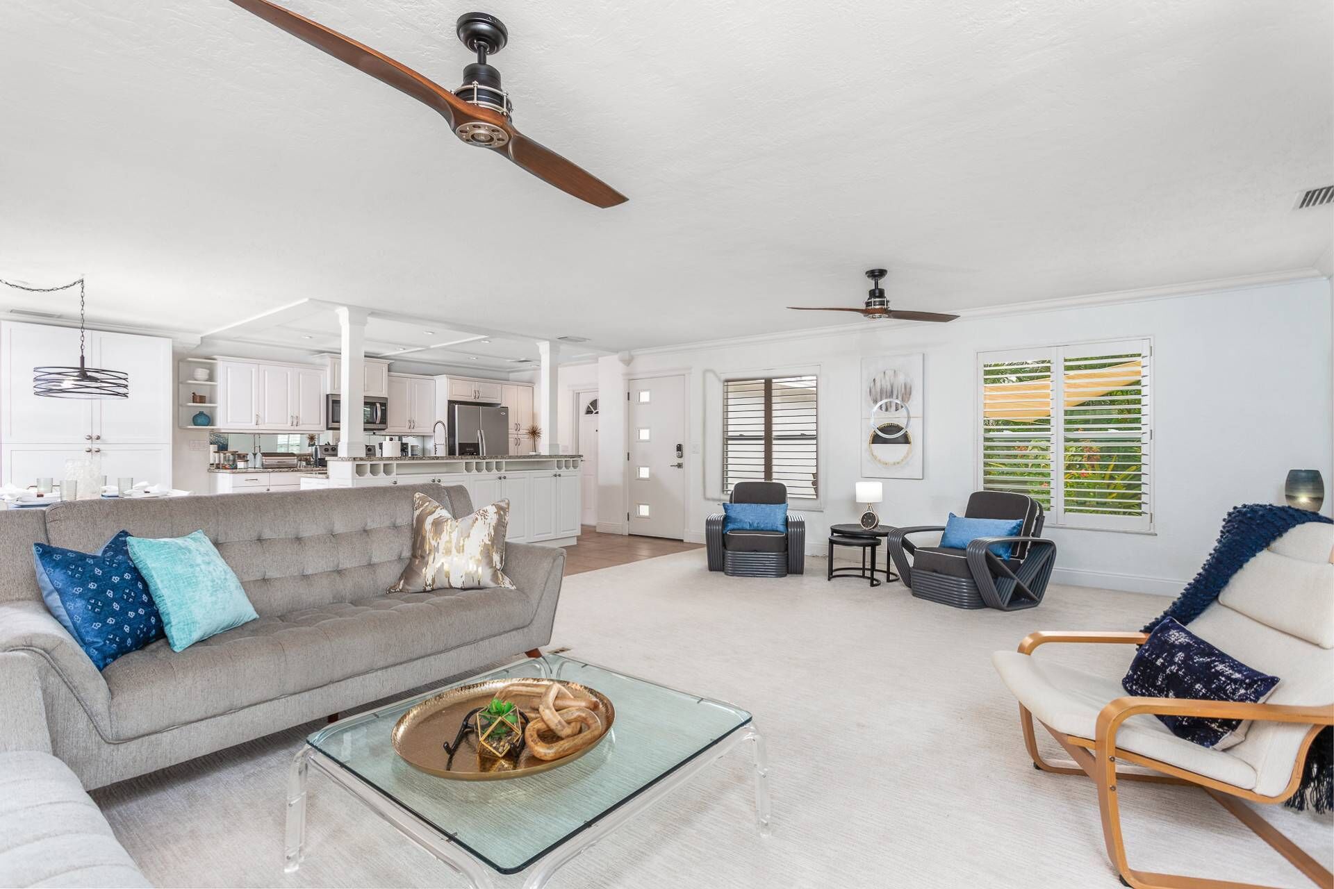 A spacious living room with a grey sofa, a glass coffee table, and a dining area with white cabinets and a kitchen in the background.