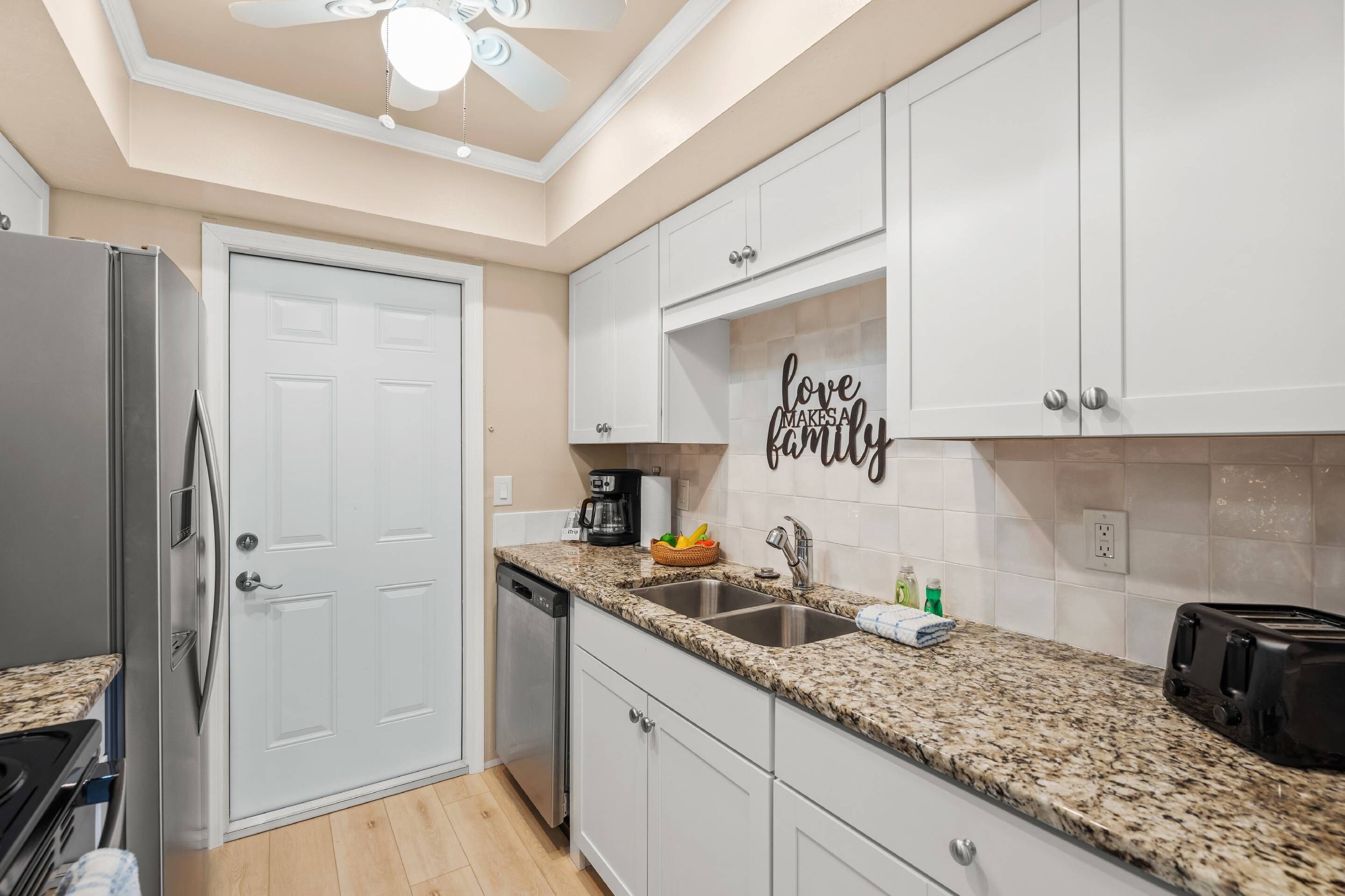 A modern kitchen with white cabinets, granite countertops, a built-in oven, and a ceiling fan.