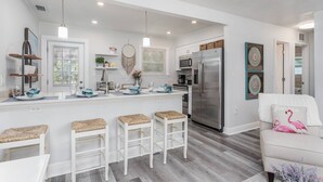 A modern kitchen with white cabinetry, a stainless steel refrigerator, and a bar area with stools. - Seagrass Cottage (Sarasota)