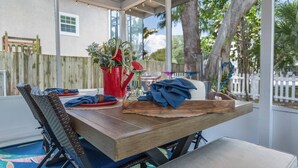 A covered patio with a wooden table, chairs, and a decorative vase. - Seagrass Cottage (Sarasota)
