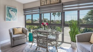 A sunlit room with a large sliding glass door, a gray sofa, a wicker table with a vase of flowers, and a ceiling fan. - Vista Hermosa Third Floor - Elevator (Siesta Key)