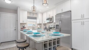A modern kitchen with white cabinets, stainless steel appliances, and a central island with stools. - Vista Hermosa Third Floor - Elevator (Siesta Key)