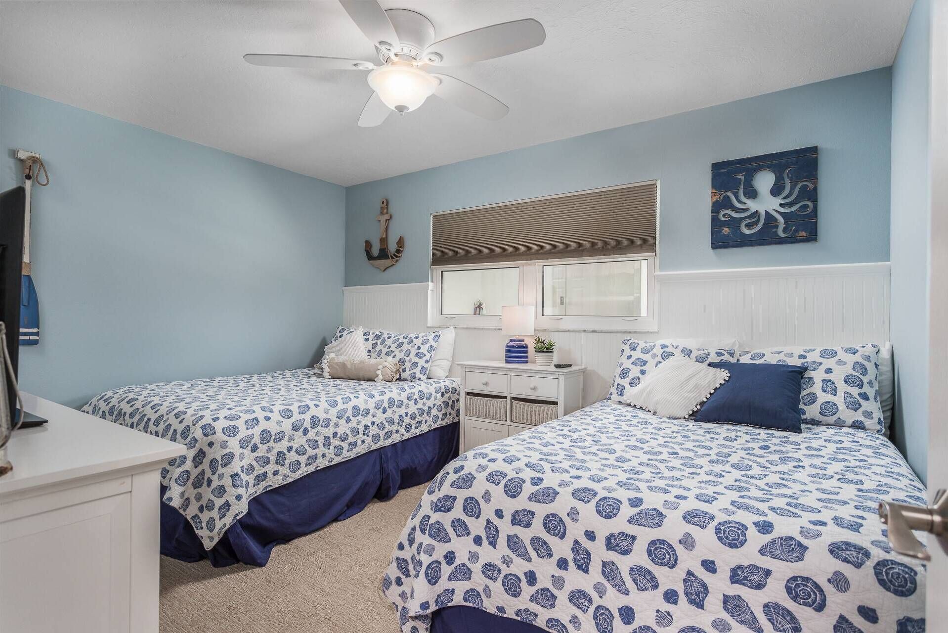 A bedroom with two beds, a ceiling fan, a nightstand, and a wall-mounted anchor decoration.