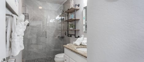 Un baño moderno con cabina de ducha de vidrio, inodoro y tocador con lavabo.