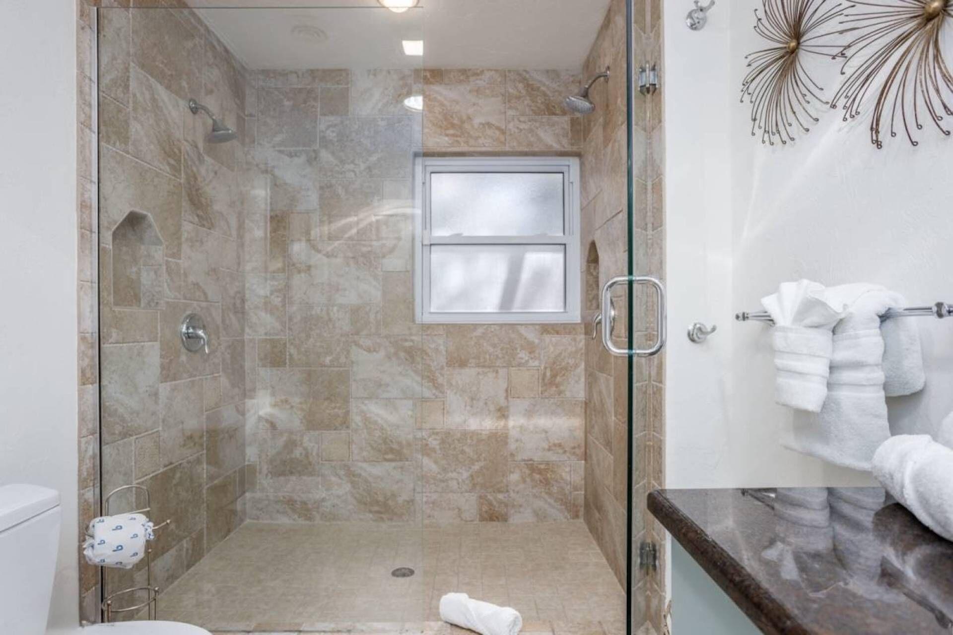 Une douche avec une porte en verre, une fenêtre et un porte-serviettes avec des serviettes.