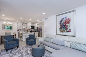 A modern living room with a grey sofa, two blue armchairs, a patterned rug, and a framed botanical print on the wall. - Sea La Vie Villa With Tropical Views (Sarasota)