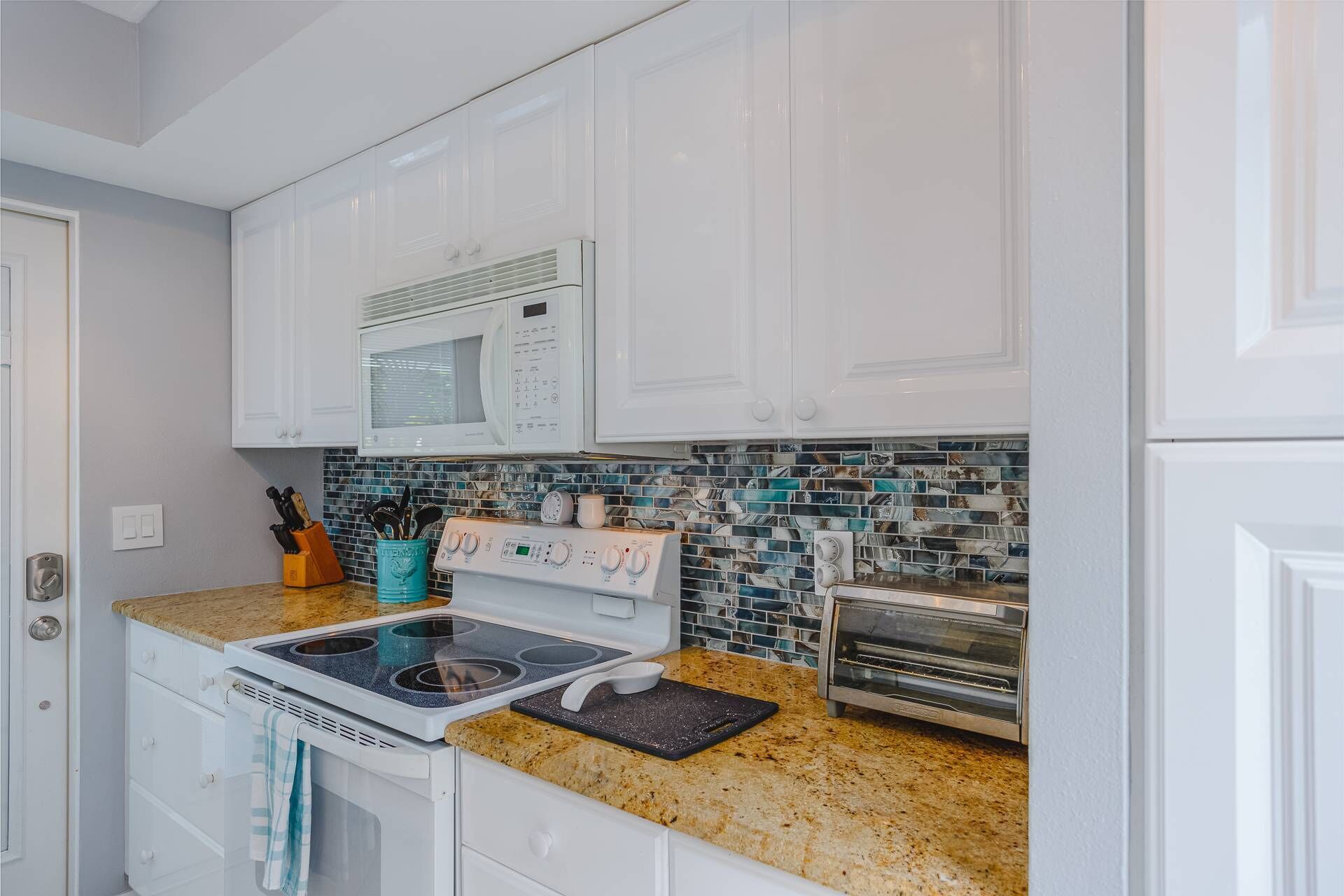 A kitchen with white cabinets, a microwave, a stove, a toaster, and a tiled backsplash.