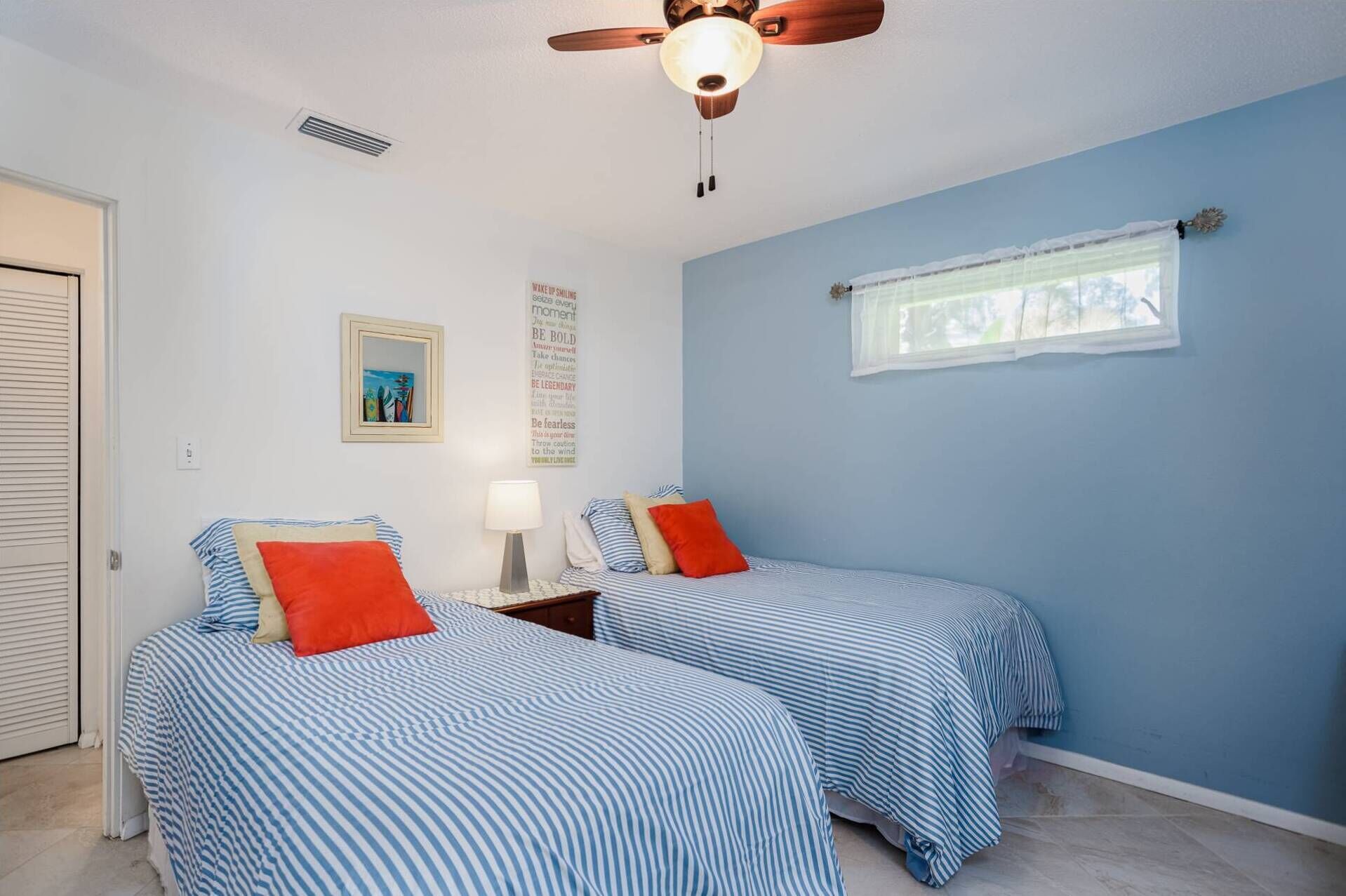 A bedroom with two beds, a ceiling fan, a window with sheer curtains, and motivational posters on the wall.