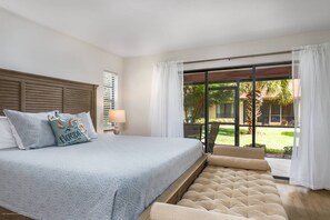 Een slaapkamer met een groot bed, een raam met gordijnen, uitzicht op de omgeving en een klein tafeltje met een lamp.