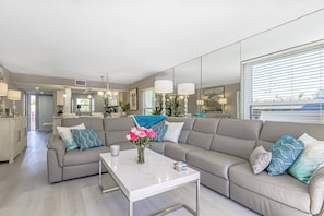 A modern living room with a grey sectional sofa, a white coffee table, and a vase of pink flowers. - Siesta Breakers on Crescent Beach (Siesta Key)