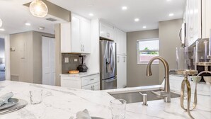 A modern kitchen with white cabinets, a stainless steel refrigerator, a built-in oven, a marble countertop, and pendant lighting.