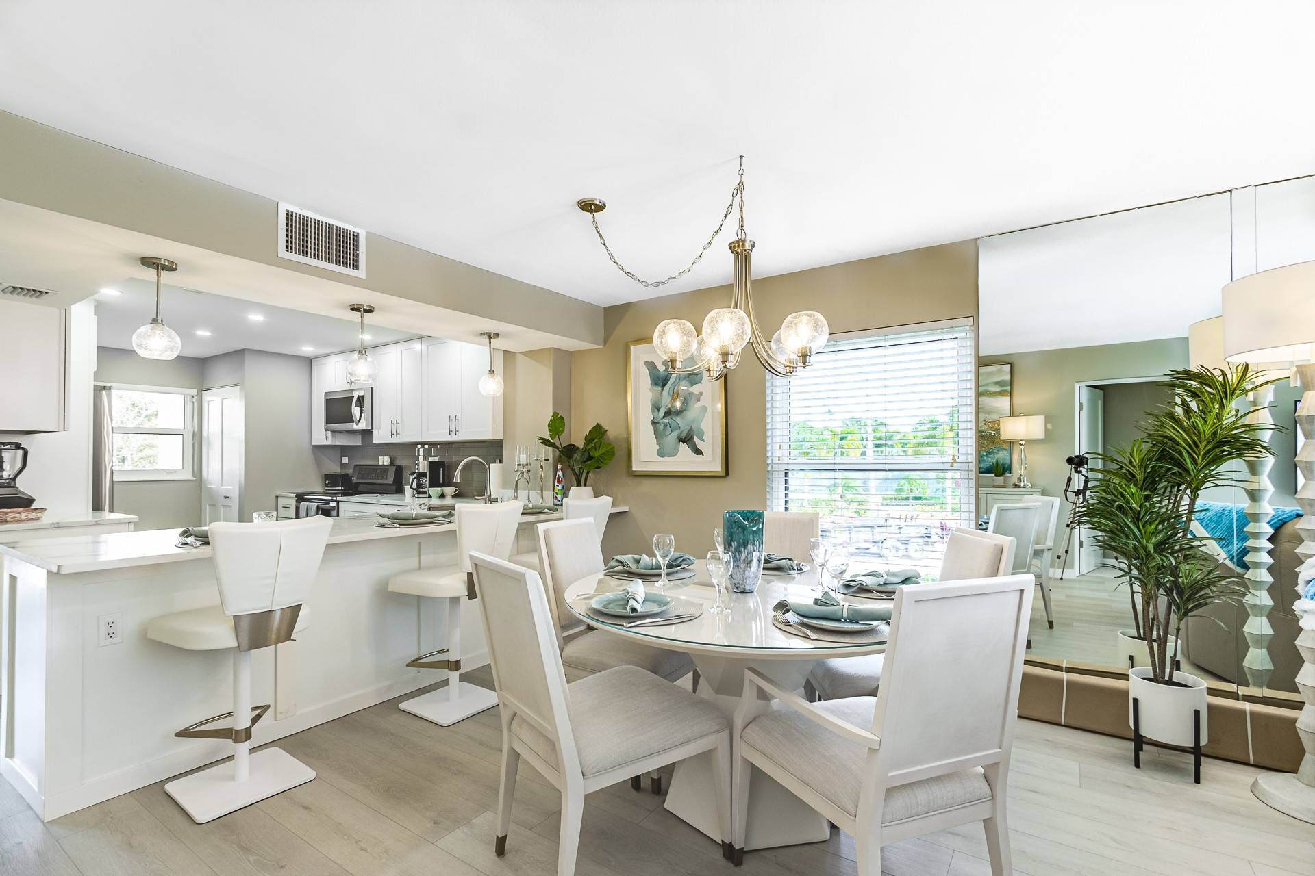 Una cocina moderna con armarios blancos, un comedor con mesa de vidrio y un ventanal con persianas.