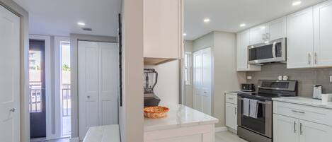 A modern kitchen with white cabinets, a built-in microwave, a stove, and a blender on the countertop.