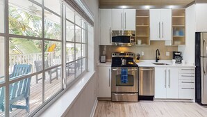 A modern kitchen with white cabinets, stainless steel appliances, and a large window overlooking a deck. - Beach Club Modern Condo C Bldg (Siesta Key)