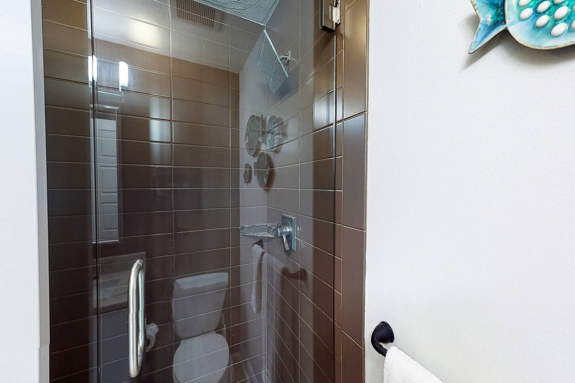 A bathroom with dark brown tiles, a glass shower enclosure, a toilet, and a towel rack.