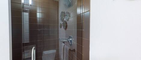 A bathroom with dark brown tiles, a glass shower enclosure, a toilet, and a towel rack.