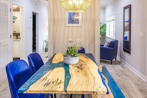A dining area with a wooden table, blue chairs, a potted plant, and a chandelier. - Beach Club Modern Condo C Bldg (Siesta Key)