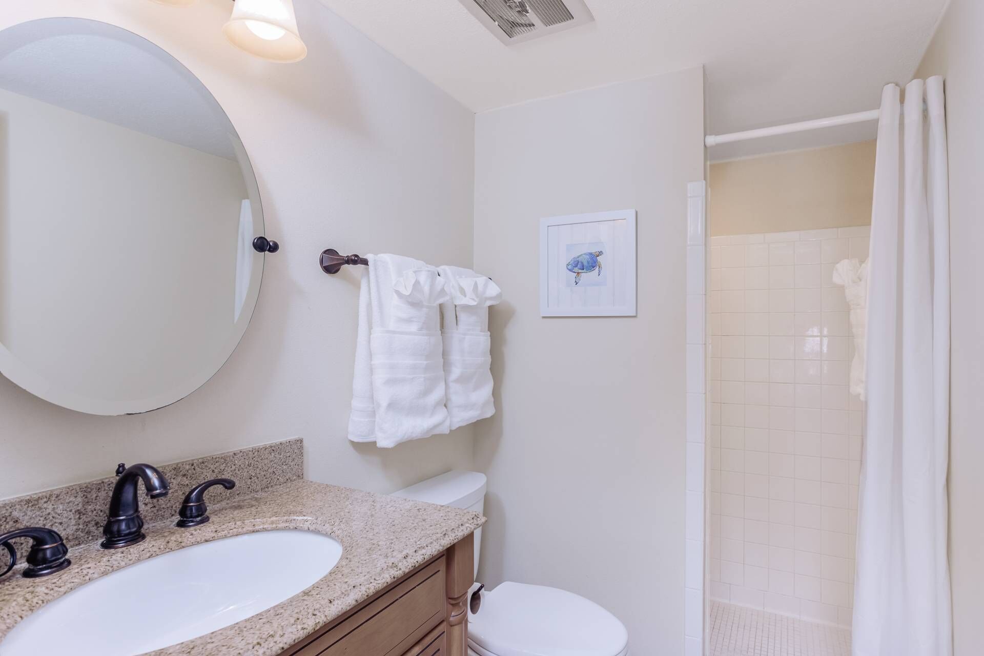 A bathroom with a round mirror, two sinks, a toilet, and a shower.