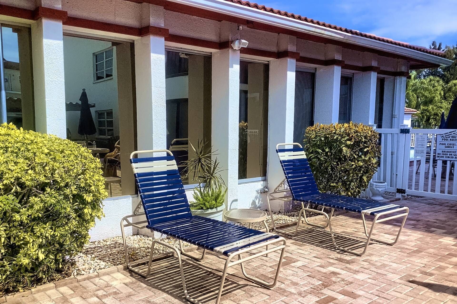 A covered outdoor seating area with two blue lounge chairs and a small table.