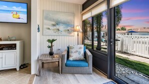 A room with a view of a beach, a wicker chair with a cushion, a small table with a lamp, and a painting on the wall. - Vista Hermosa A Few Steps to the Heated Pool (Siesta Key)