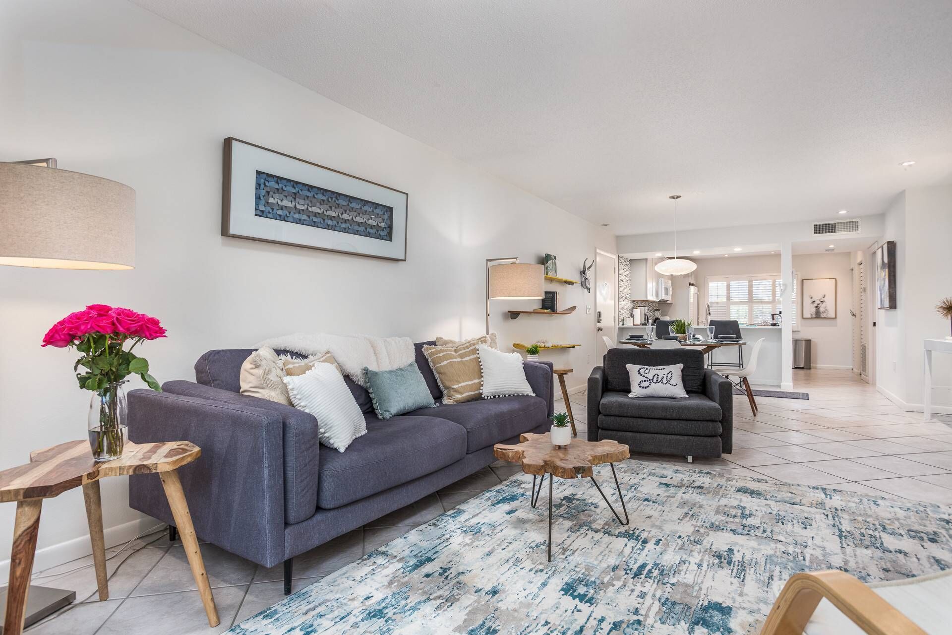 Een moderne woonkamer met een grijze bank, een houten salontafel en een blauw, gestreept vloerkleed.