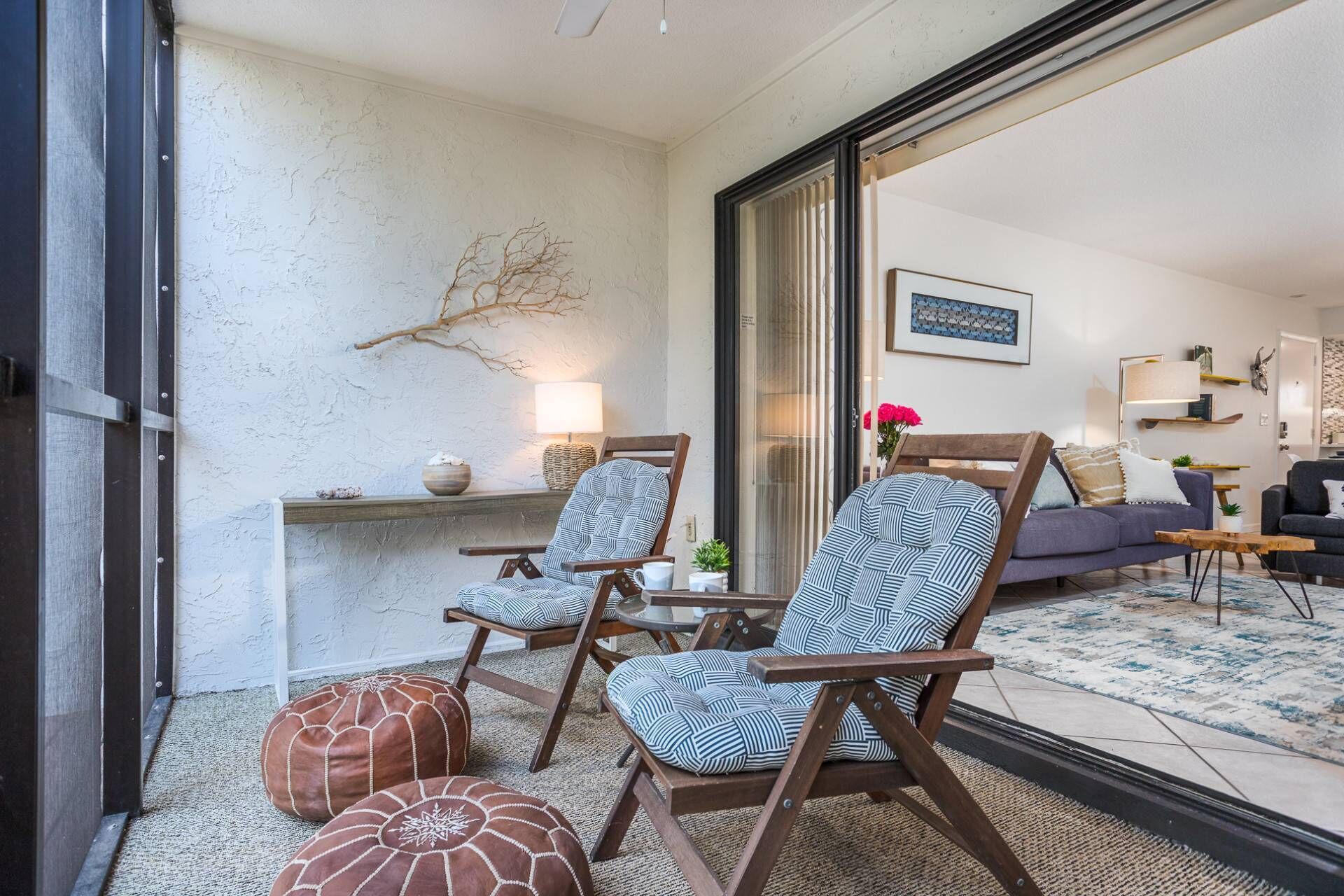 A cozy living area with two wooden chairs, a sofa, and a coffee table. A branch decor is mounted on the wall, and a lamp is on a side table.