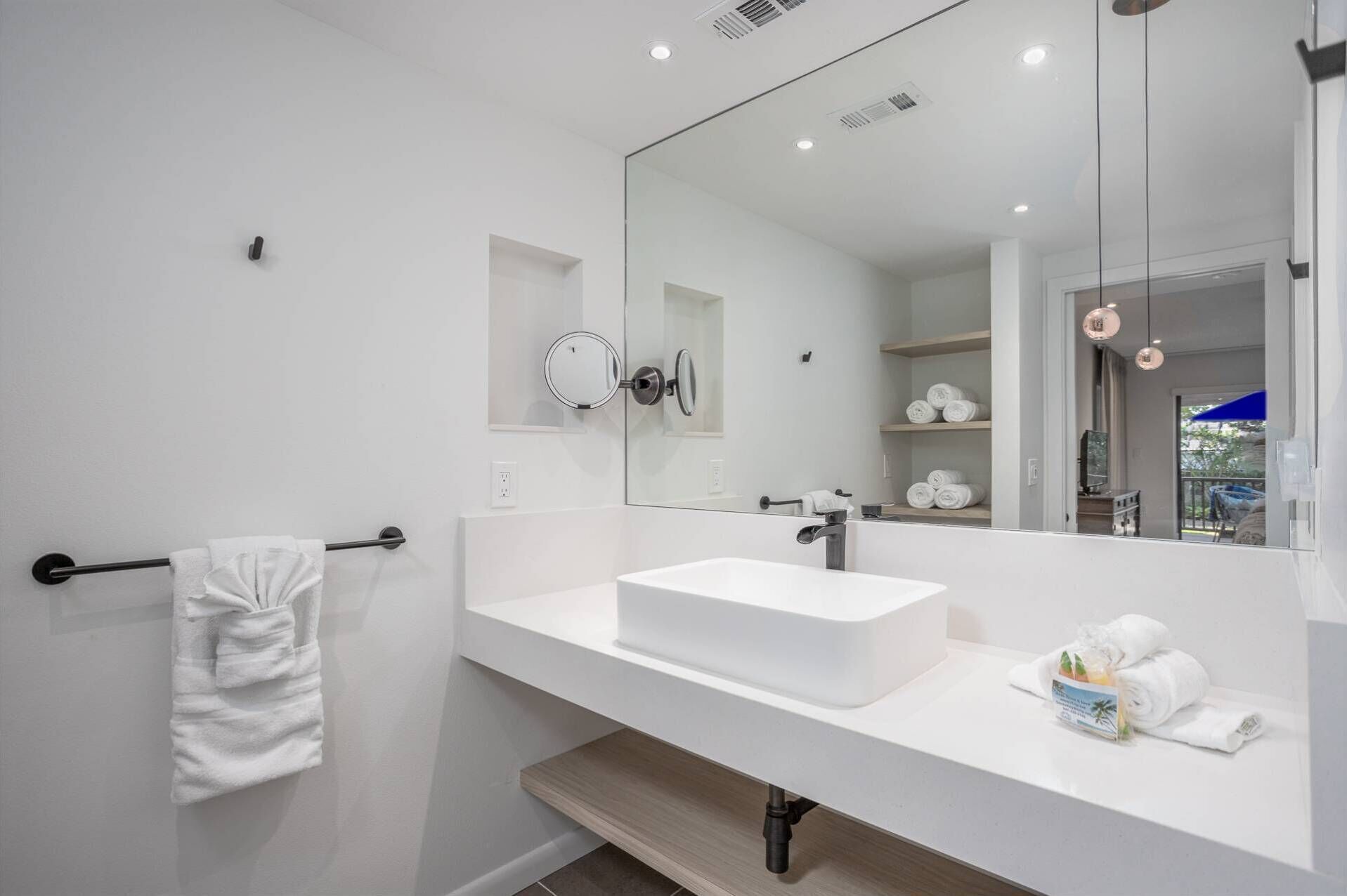 Un baño moderno con un lavamanos blanco, un espejo grande y un perchero para toallas.