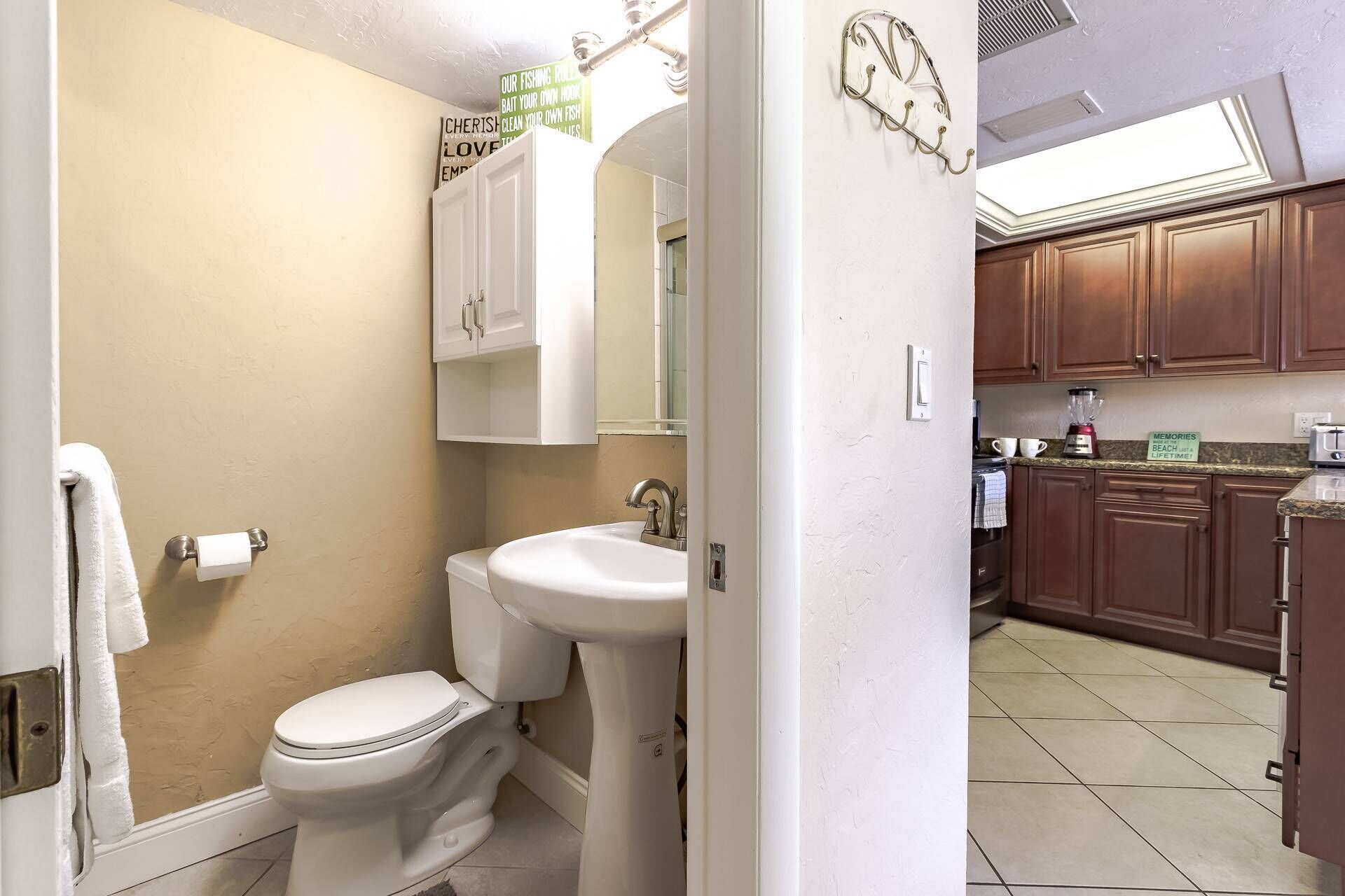 A bathroom with a toilet, sink, and mirror. There is a towel hanging on the wall. The bathroom has a beige wall and a white door.