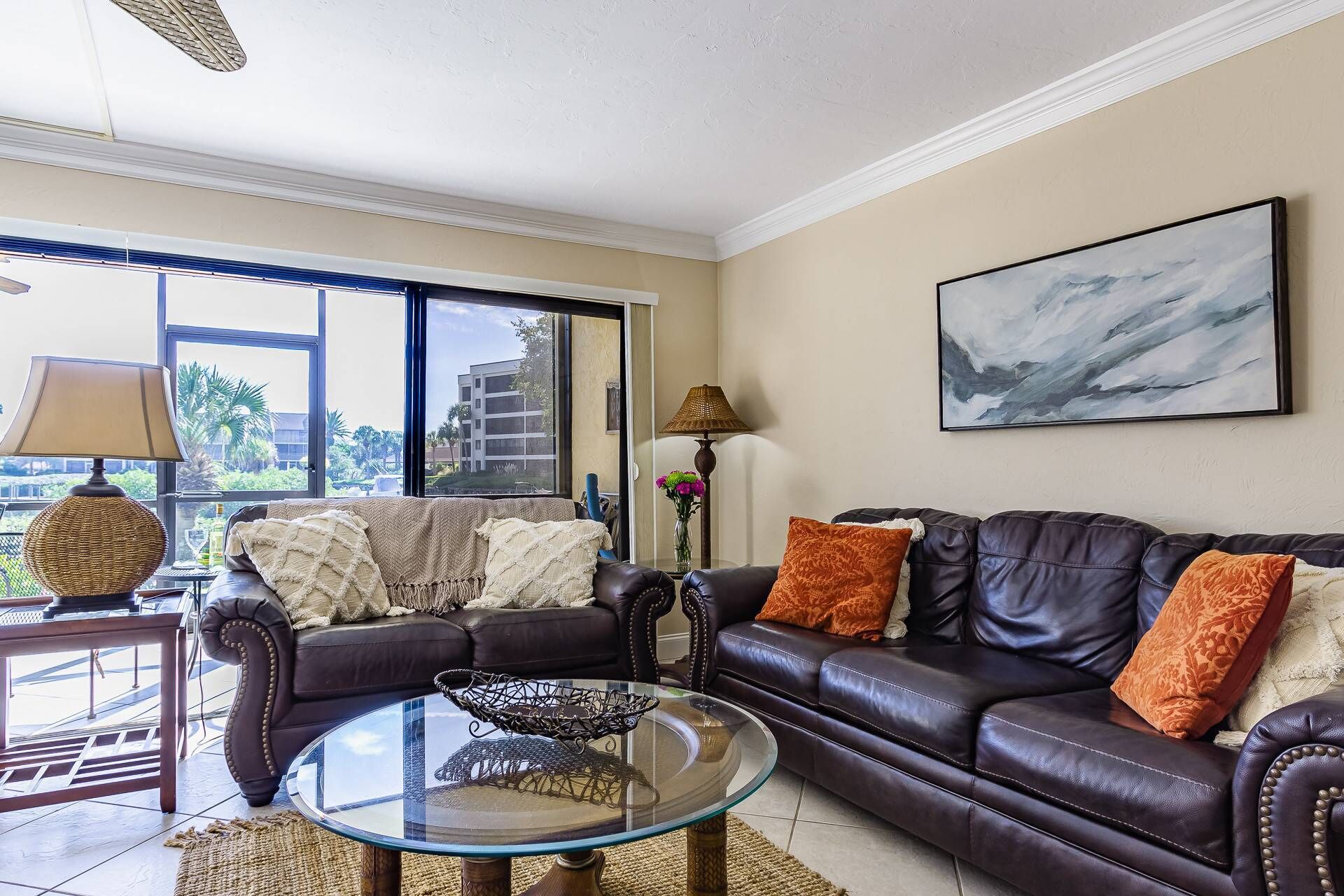 A living room with a glass coffee table, leather sofas, and a large window with a view of buildings and greenery.