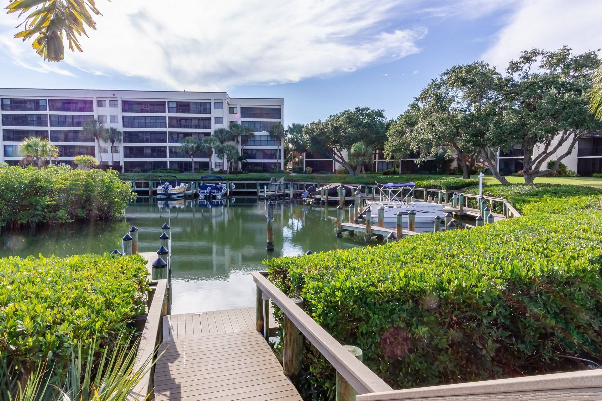 A marina with boats docked, a wooden dock leading to the water, and a modern building in the background.