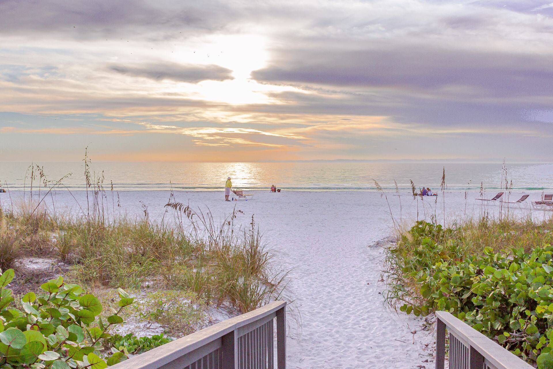 A beach path leading to the sea with a wooden railing on one side and vegetation on the other.