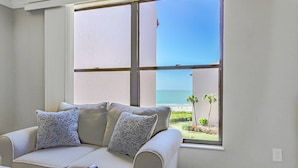 Ein Zimmer mit großem Fenster und Blick auf Strand und Palmen.