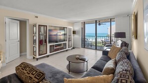 Ein geräumiges Wohnzimmer mit großem Fernseher, einem Balkon mit Meerblick und einer gemütlichen Sitzecke.