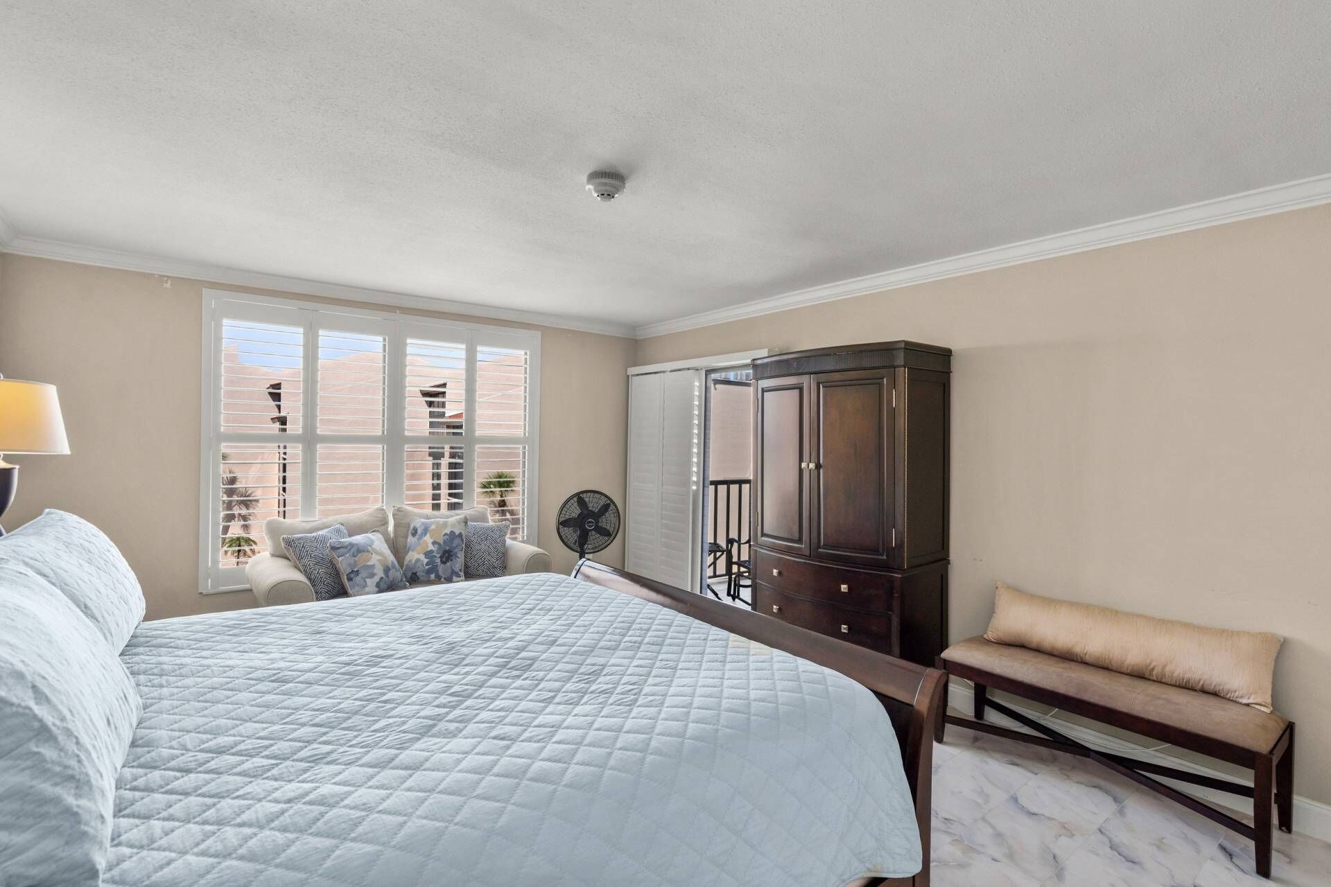 A bedroom with a bed, a nightstand, a dresser, a bench, and a window with blinds.