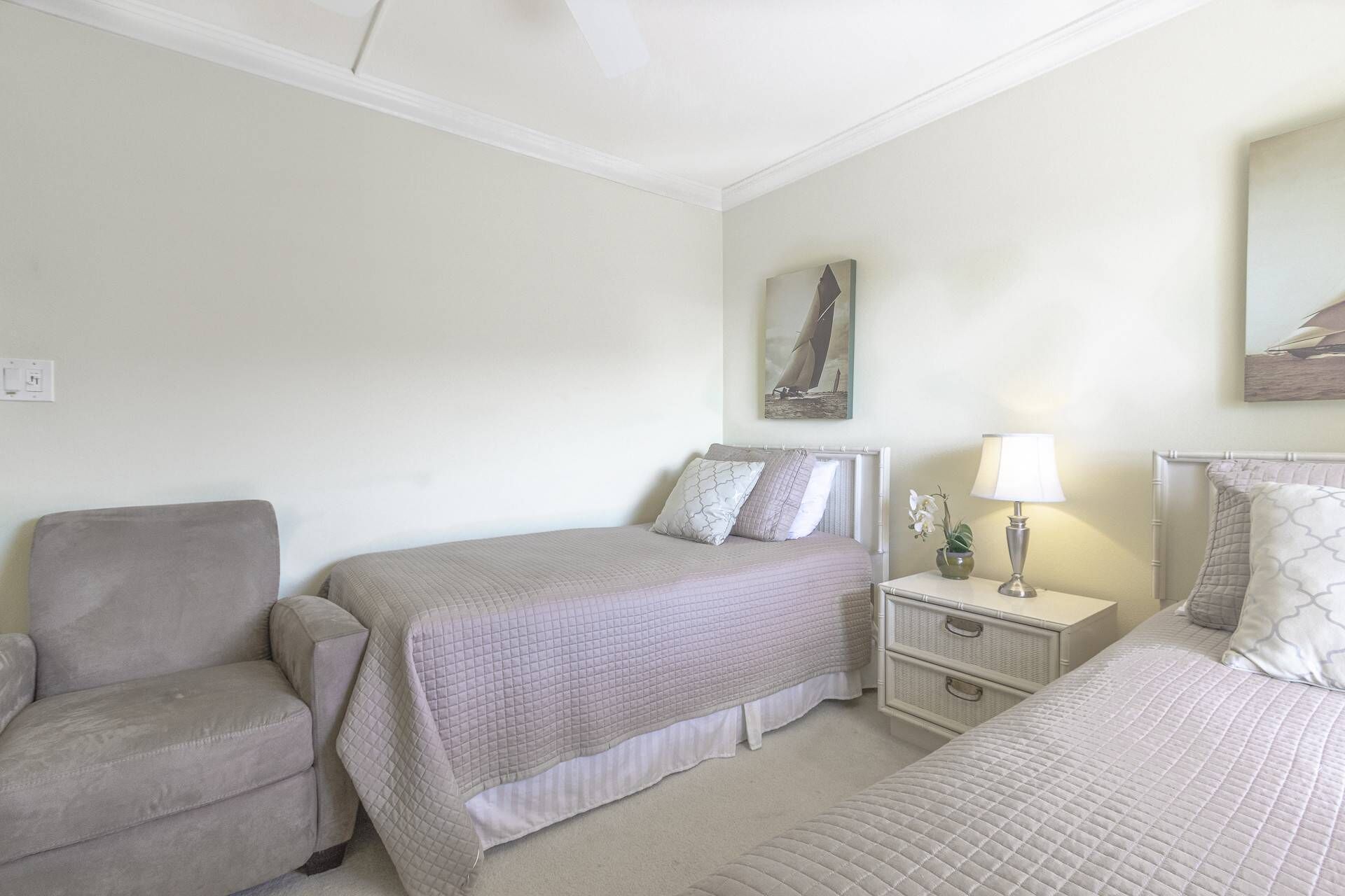 Un dormitorio con dos camas, una silla, una mesita de noche con lámpara y un cuadro en la pared.