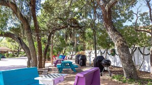Een buitenterras met picknicktafels, een barbecue en sfeerverlichting.