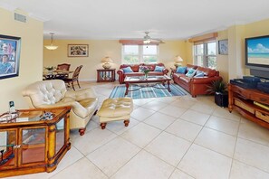 Ett rymligt vardagsrum med en soffa klädd i läder, ett soffbord i glas och en tv som står på ett träställ.