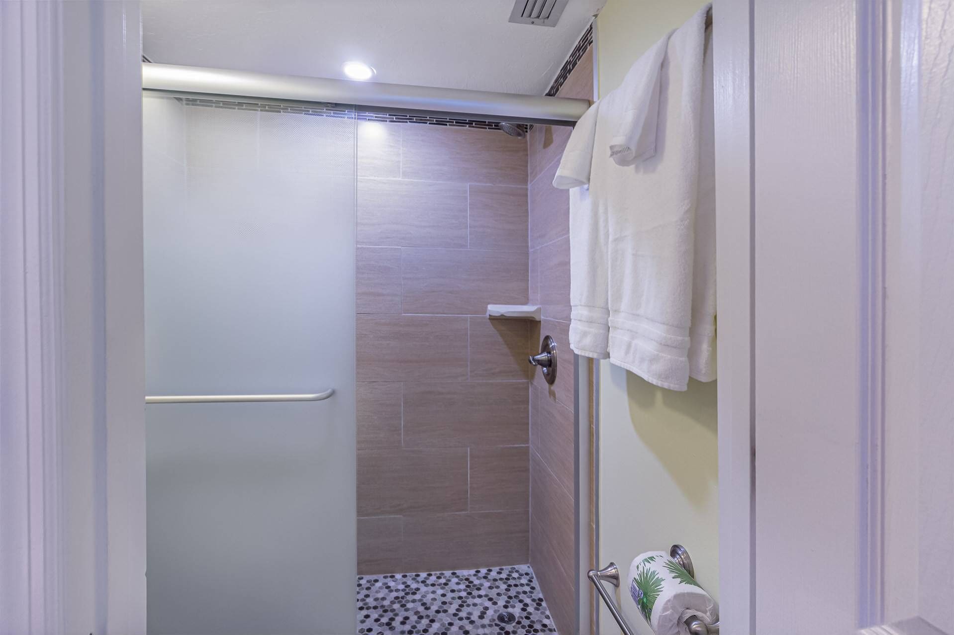 Un baño moderno con ducha, paredes de azulejos, un perchero para toallas y un dispensador de papel higiénico.