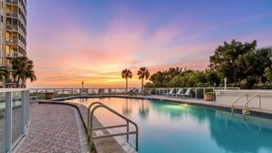 A swimming pool with a sunset view, surrounded by palm trees and a building. - Crystal Sands & Seahorses Beach Villa (Siesta Key)