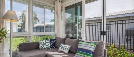 A corner sofa with patterned cushions, large windows, and a view of a fenced area outside.